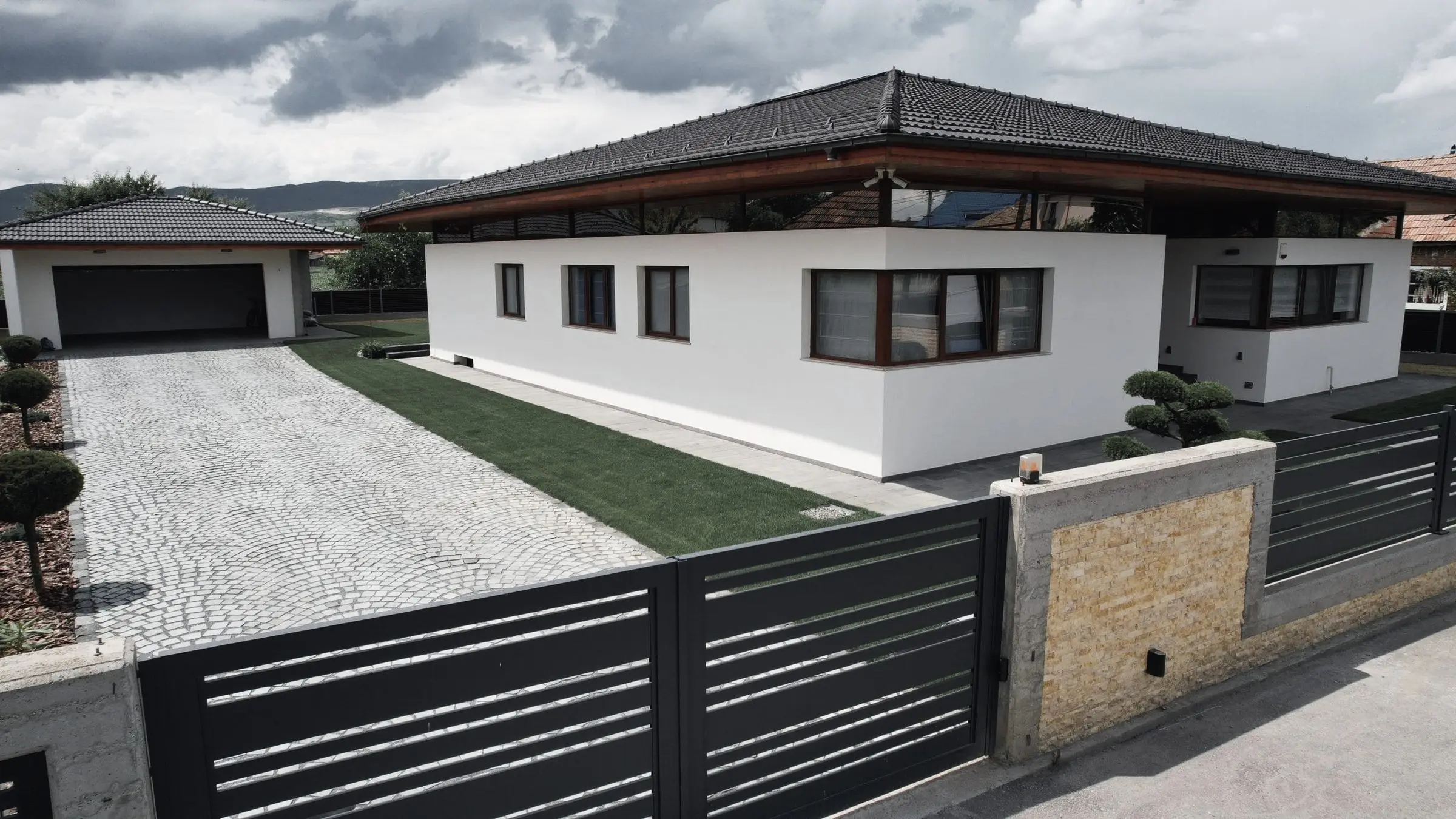 Casă albă cu acoperiș în patru ape, alee din piatră cubică și gard negru