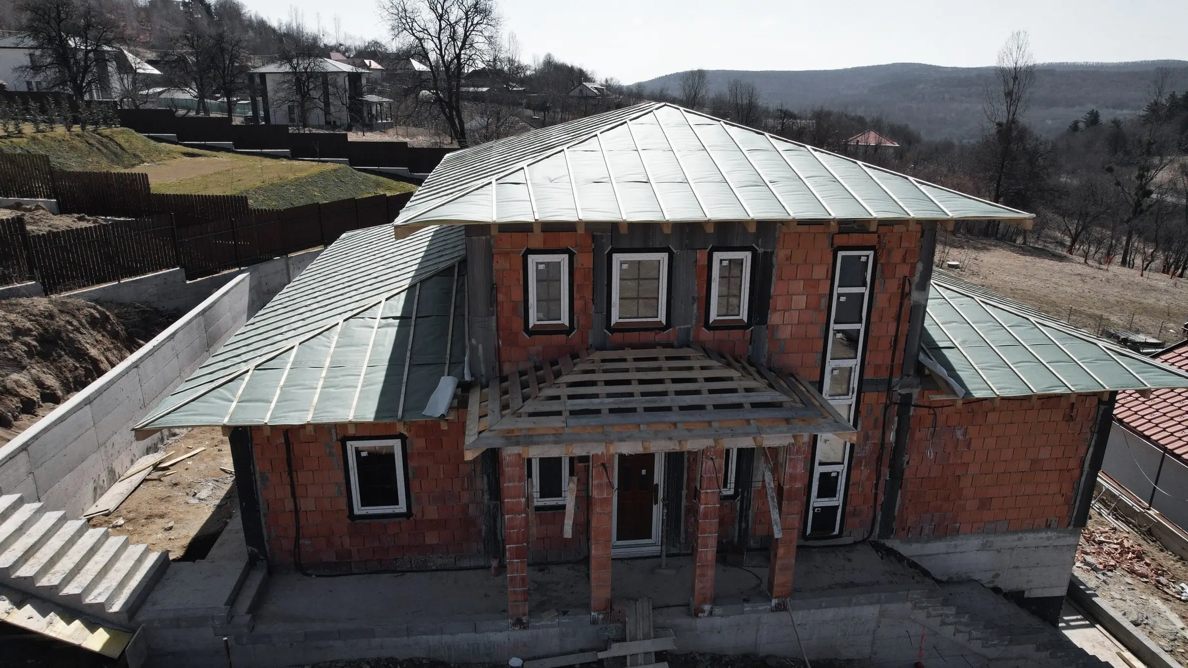 Casă din cărămidă cu acoperiș verde și pergolă din lemn, văzută din dronă