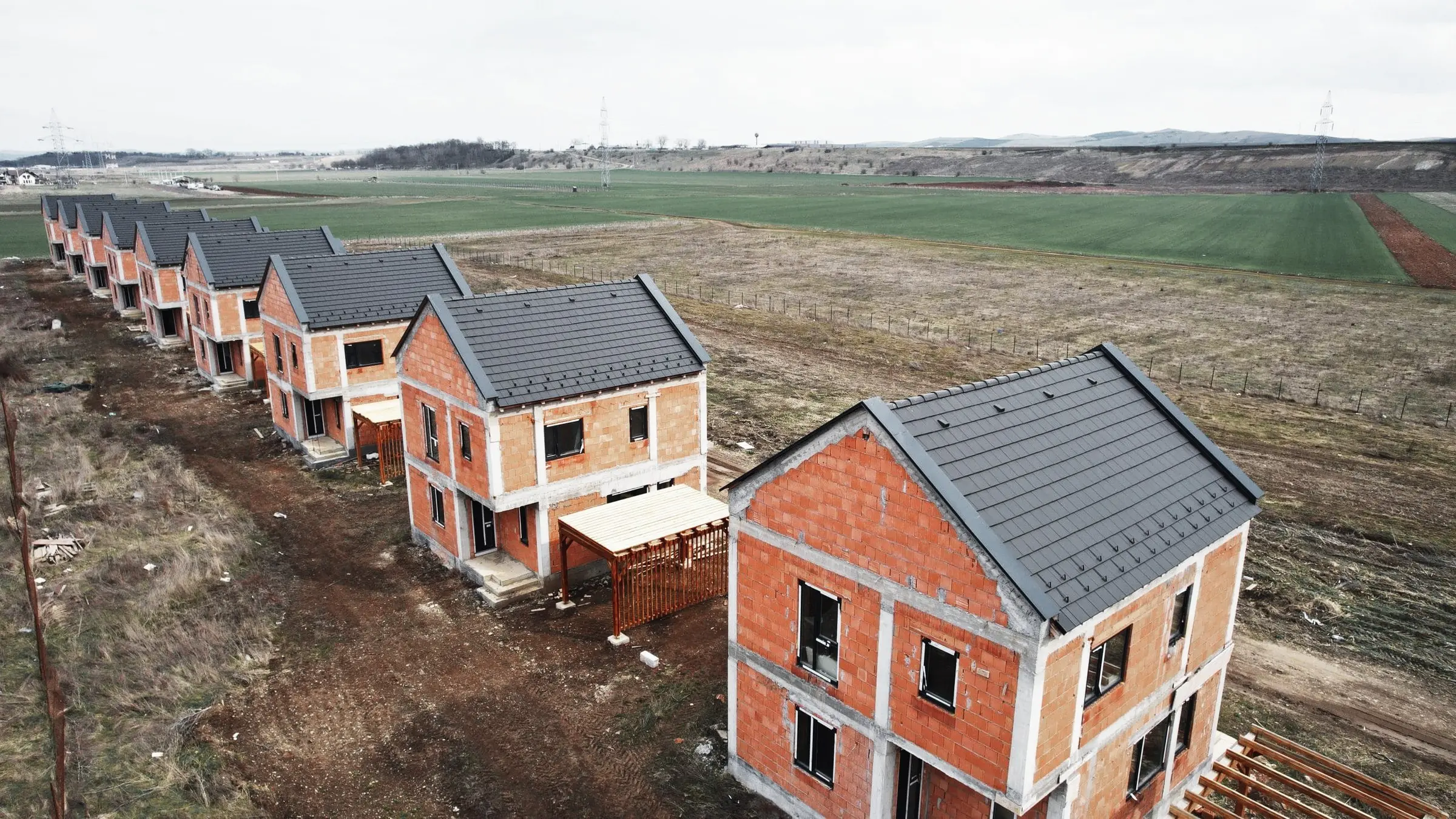 Casă din cărămidă aparentă cu acoperiș gri, în prim-plan, într-un șir de locuințe