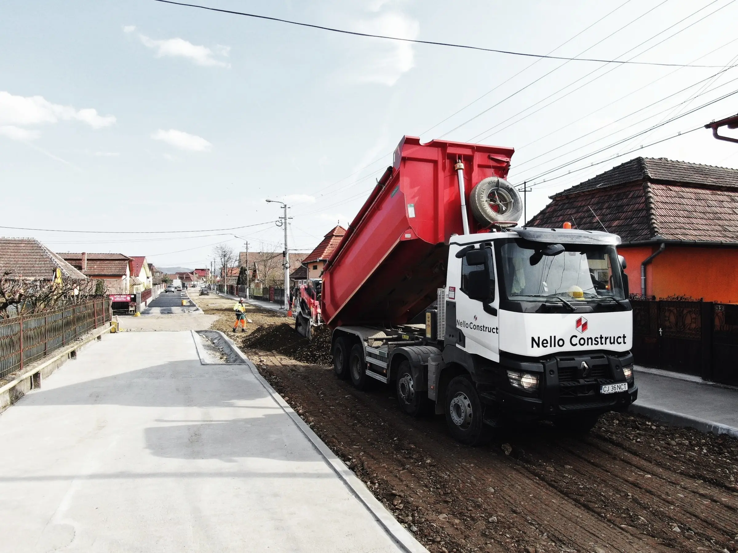 Autobasculantă Nello Construct descarcă material pe o stradă de sat în lucru