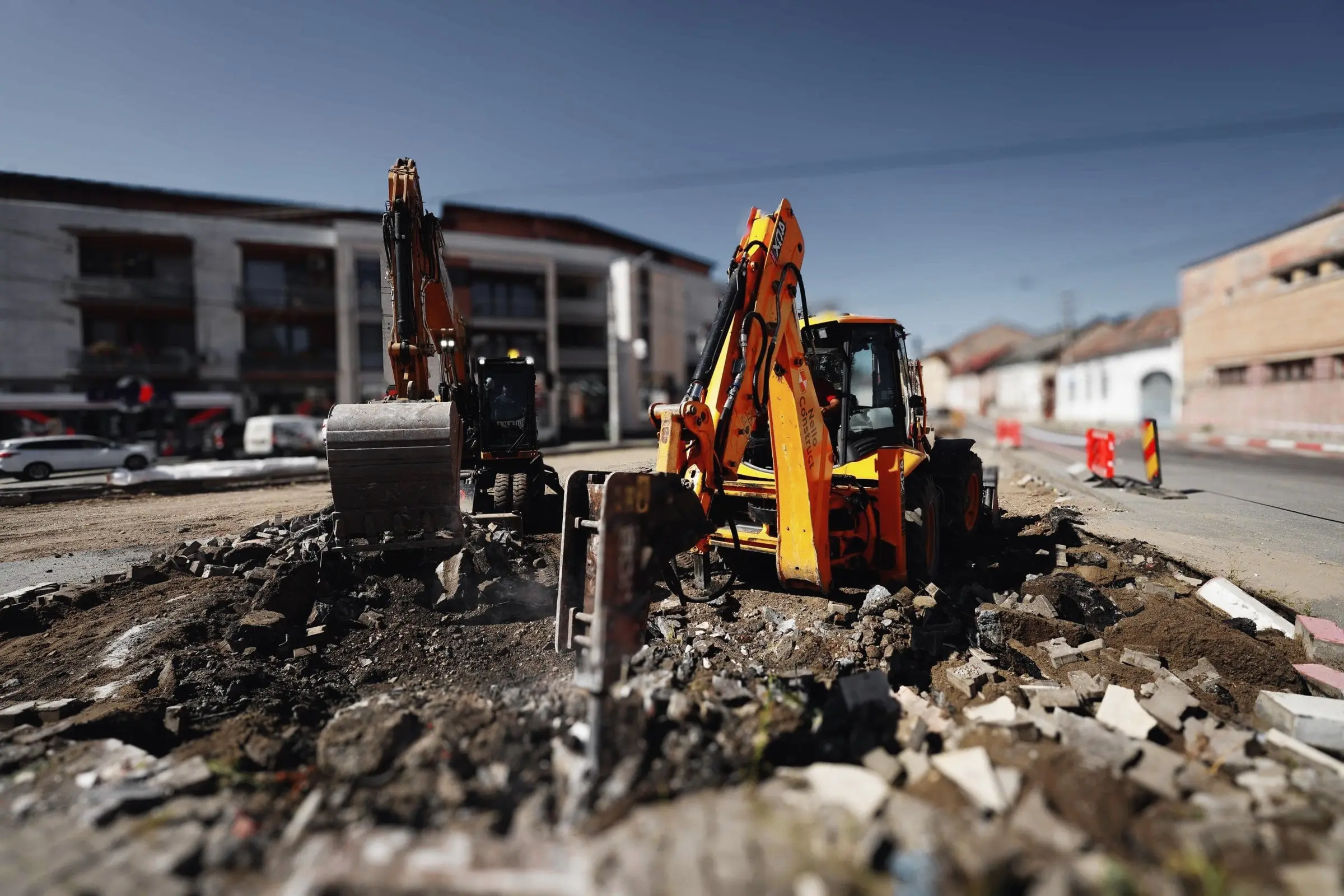 Excavator și buldoexcavator cu ciocan hidraulic sparg carosabilul unei străzi din localitate