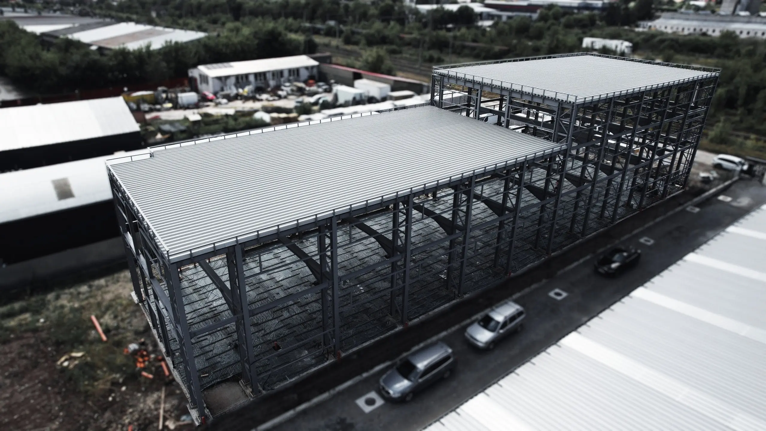 Structură metalică de hală văzută din dronă, cu acoperiș parțial montat, lângă o parcare
