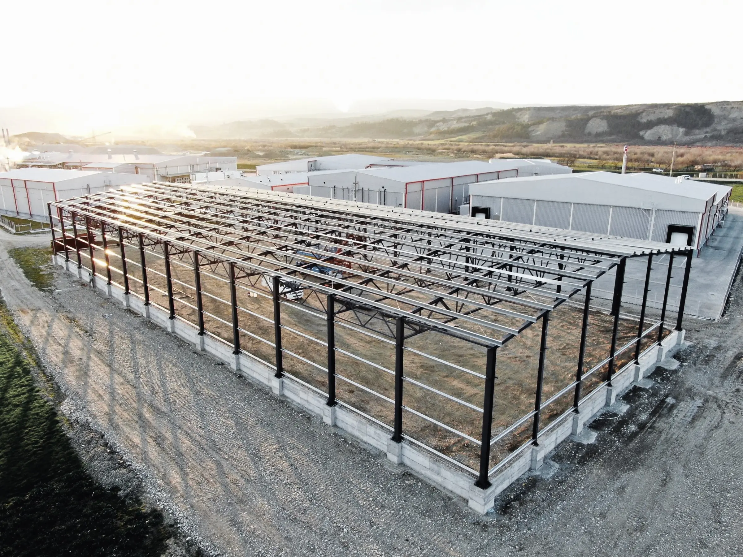 Structură metalică a unei hale cu pane de acoperiș montate, în lumina apusului