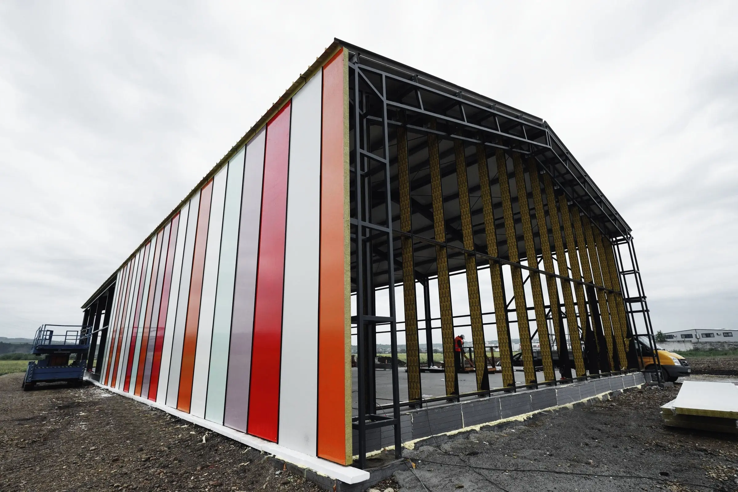 Structură metalică de hală cu panouri colorate montate parțial pe fațadă