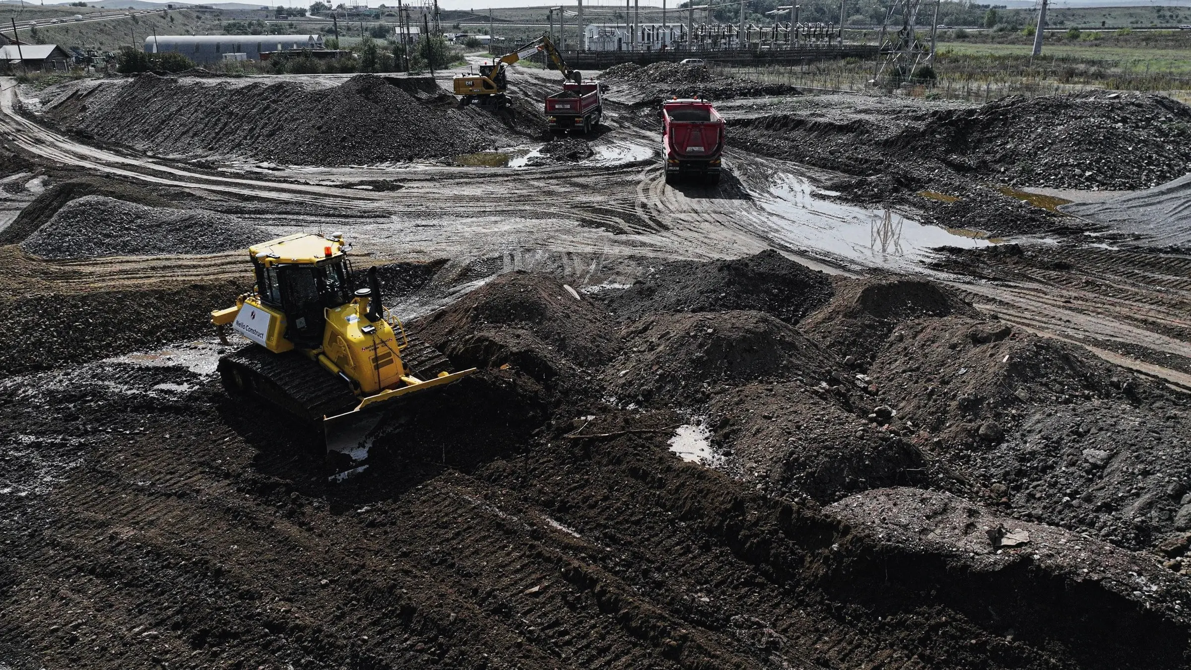 Buldozer lucrează pe un teren mocirlos, cu autobasculante în depărtare, văzut din dronă