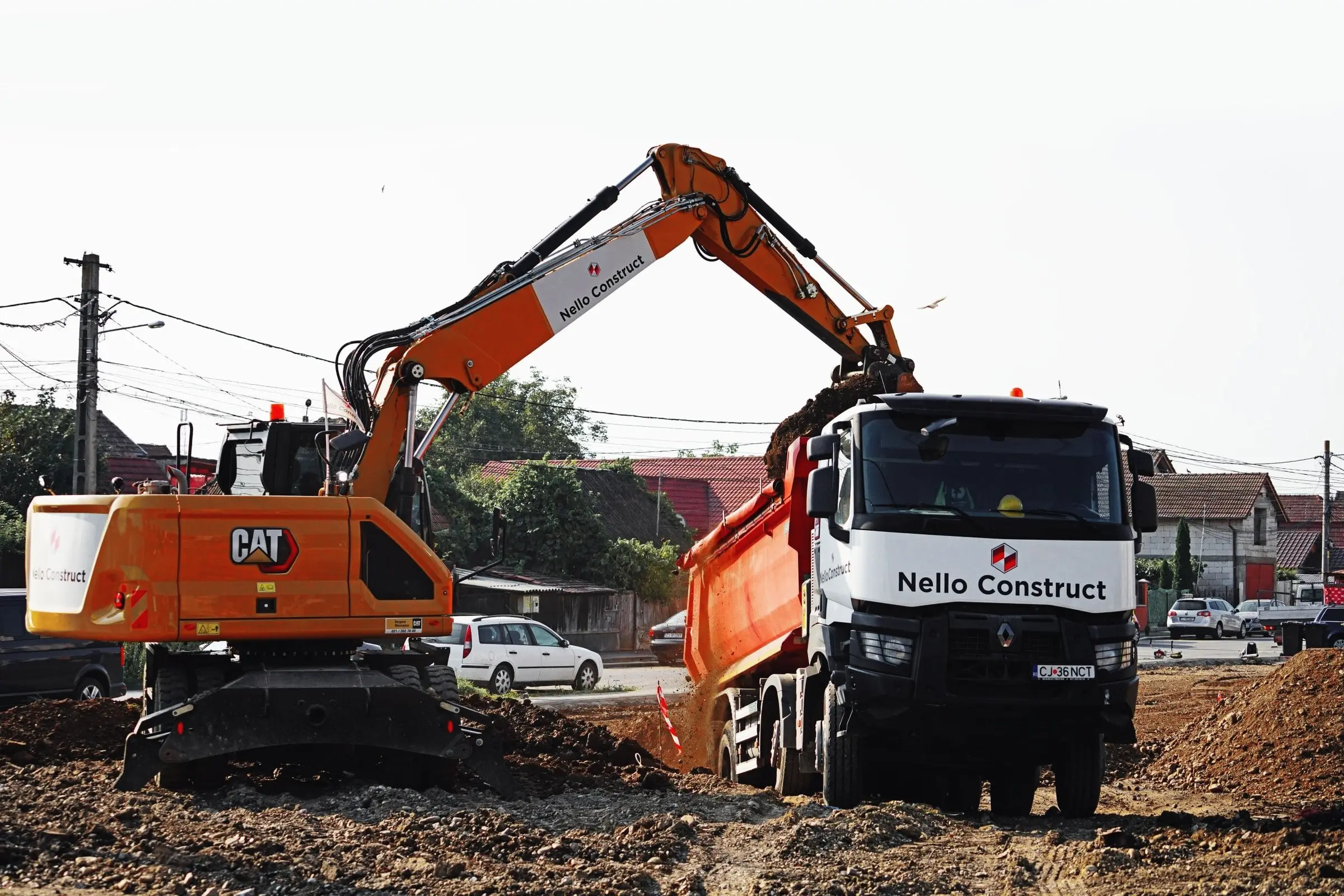 Excavator încarcă o autobasculantă Nello Construct pe un teren de pământ