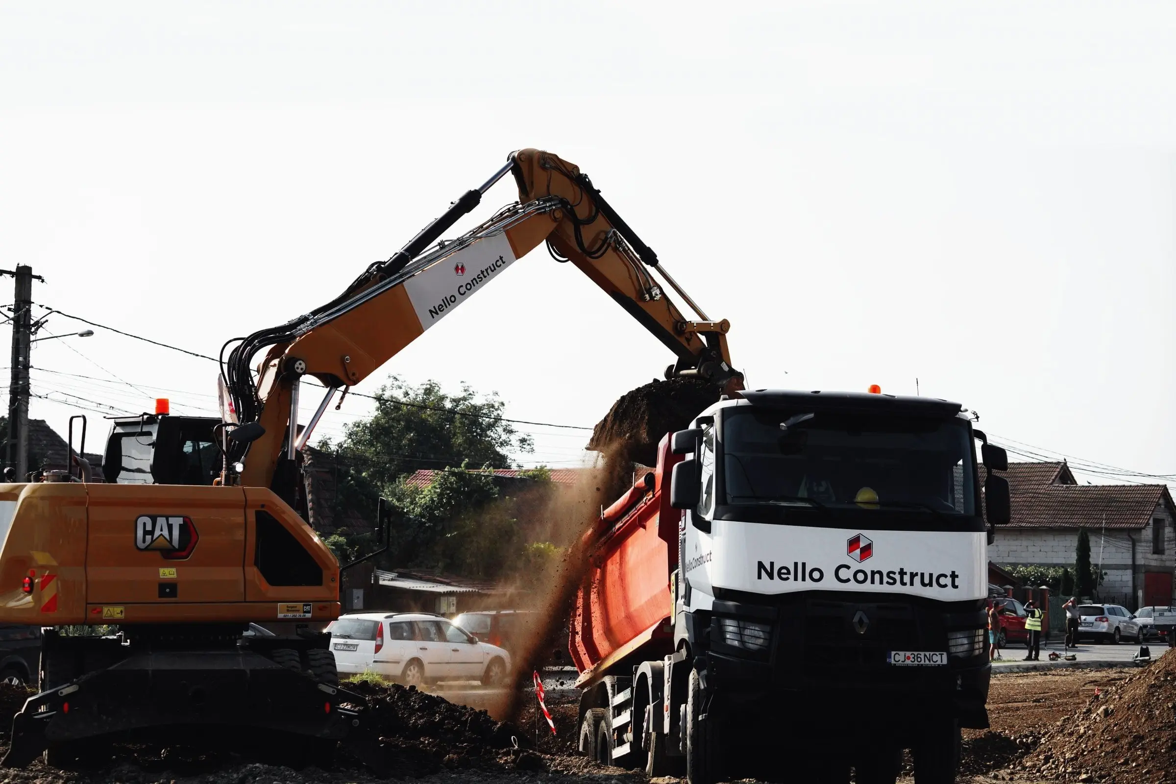 Excavator pe roți descarcă pământ într-o autobasculantă, cu praf ridicat