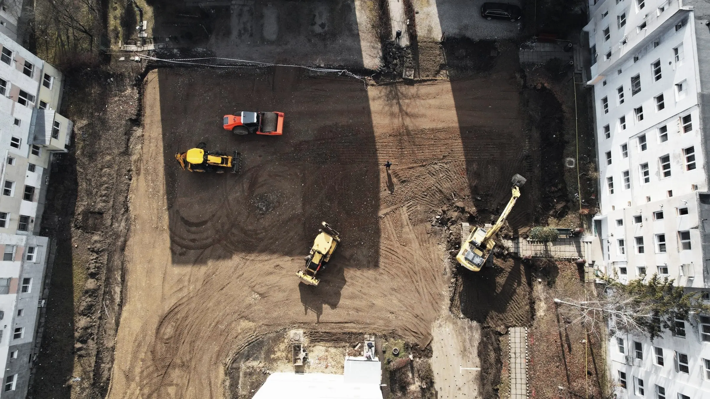 Vedere aeriană a unui șantier excavat între blocuri, cu buldoexcavatoare și utilaje la lucru