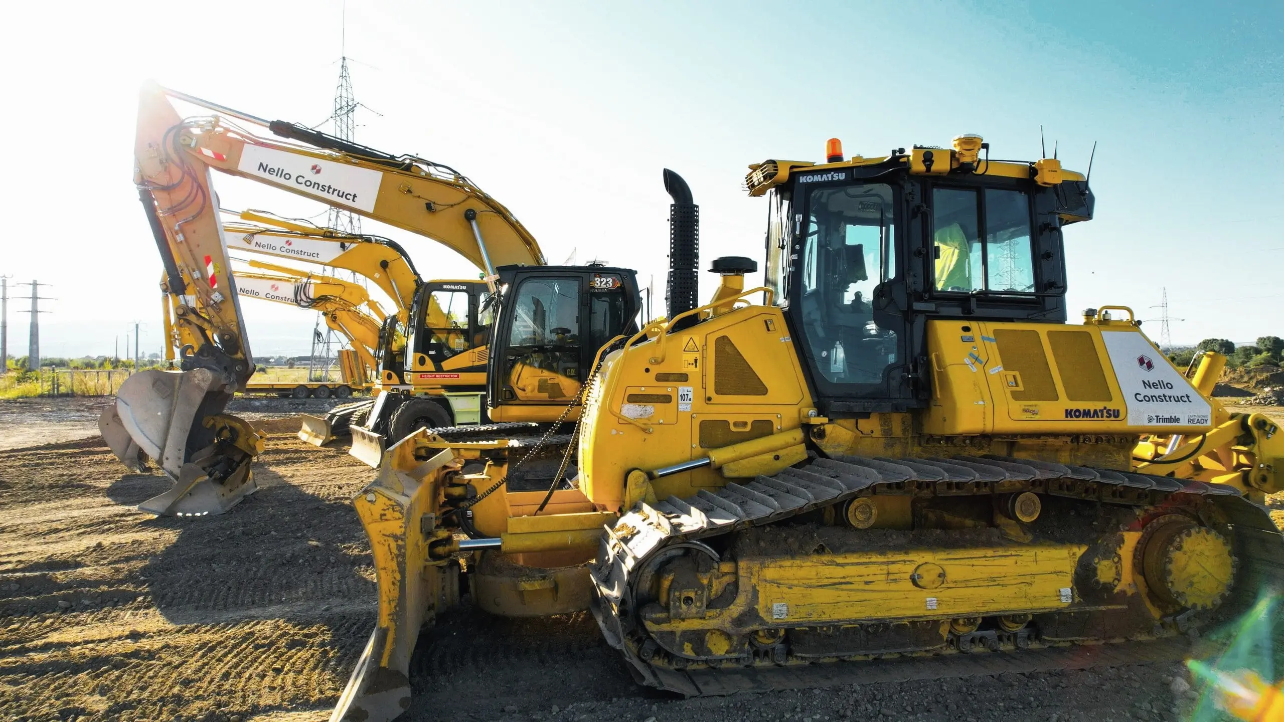 Buldozer Komatsu și excavatoare galbene marcate Nello Construct, pe un teren de șantier